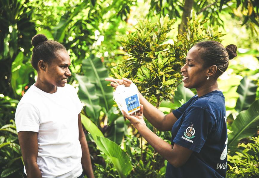 Un miembro del personal de World Mosquito Program en Vanuatu muestra a un residente cómo colgar su caja para mosquitos.